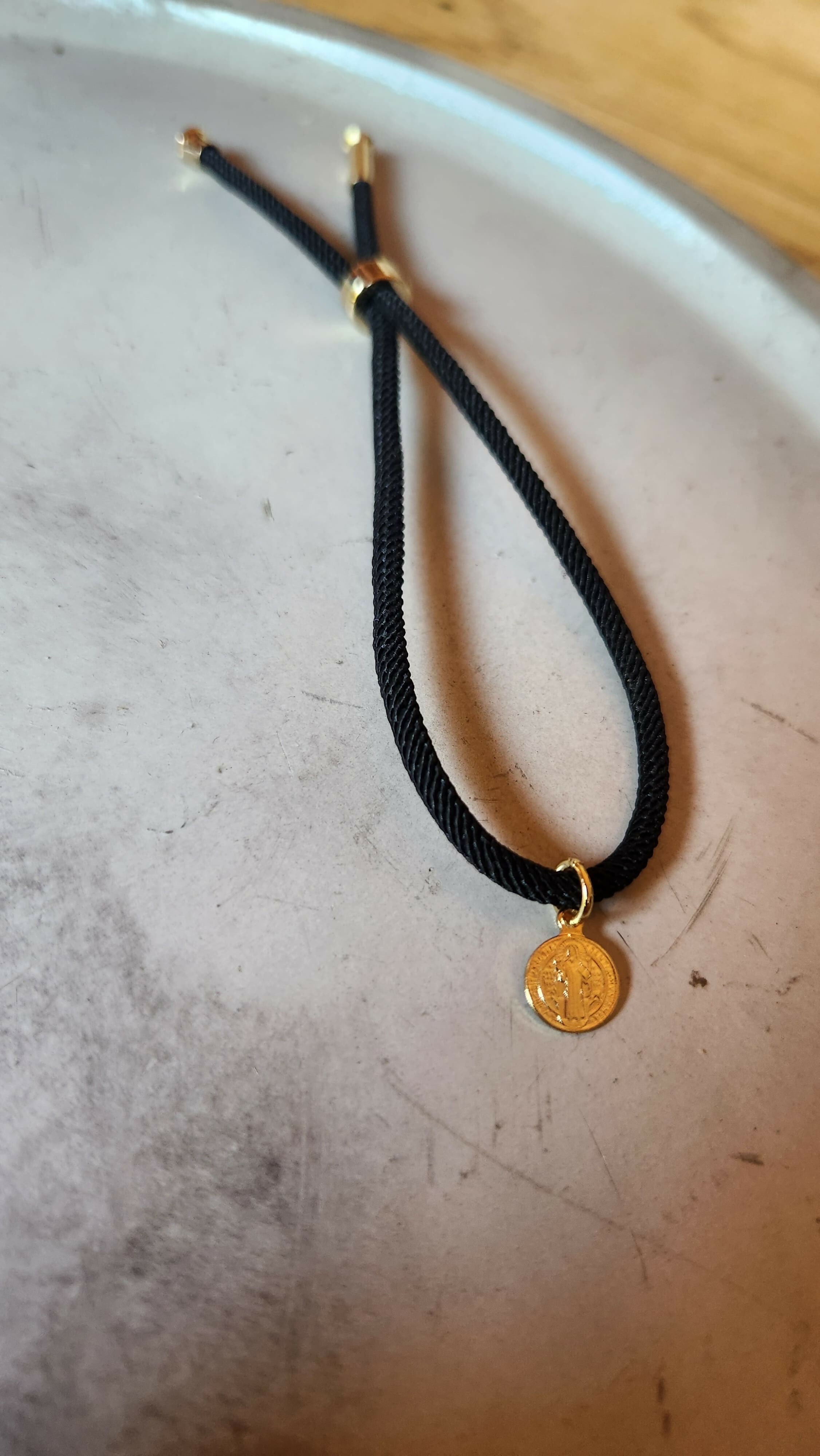 Pulsera negra tejida con San Benito baño oro