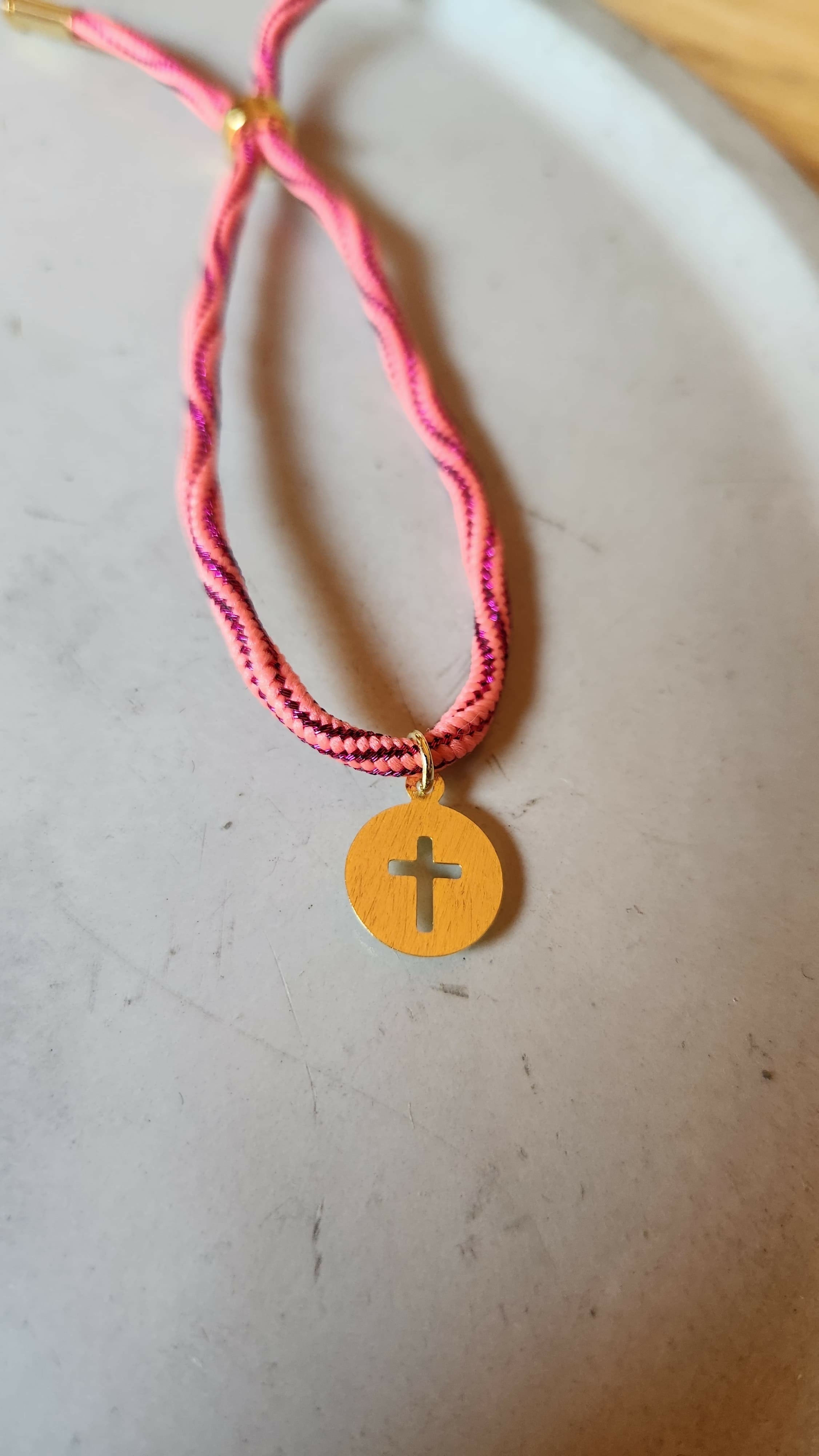 Pulsera fucsia tejida con cruz calada baño oro
